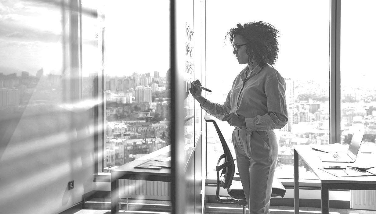 An investment advisor writes sticky notes with ideas on a whiteboard.