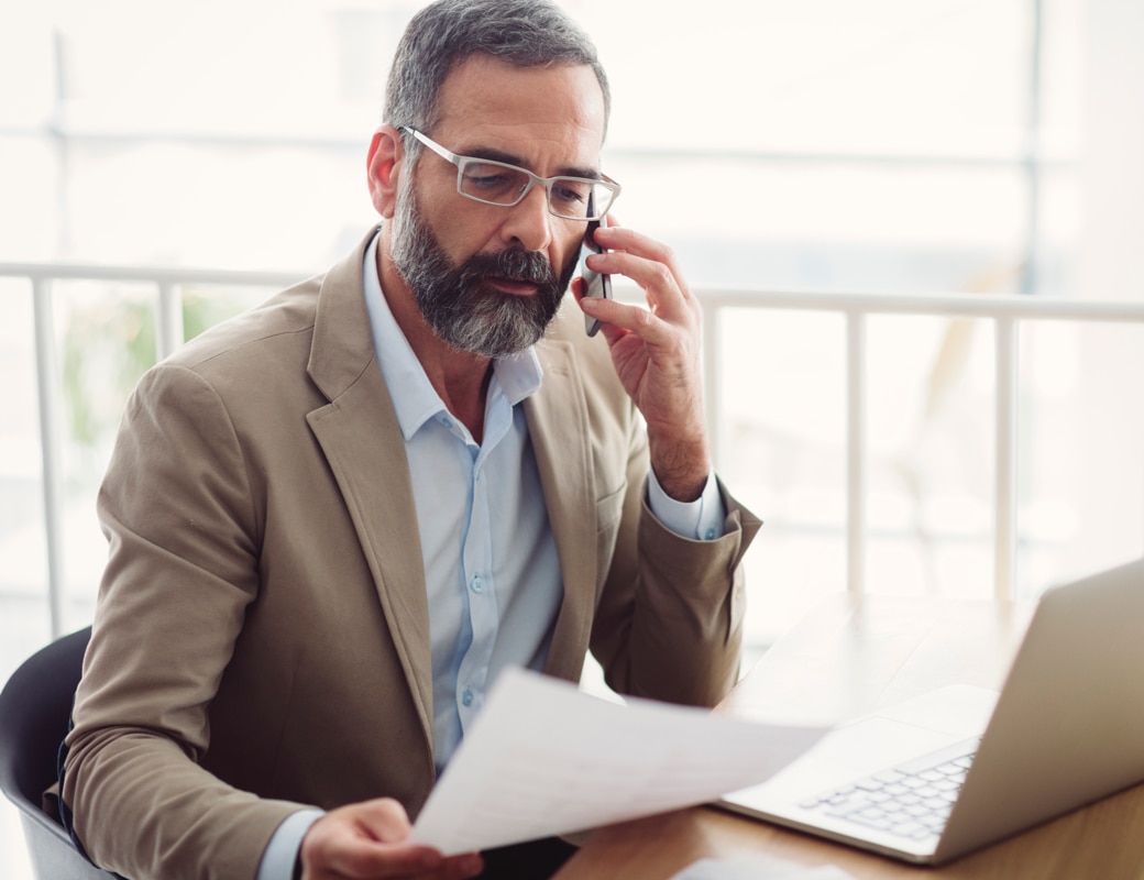 Man on phone with laptop and documents