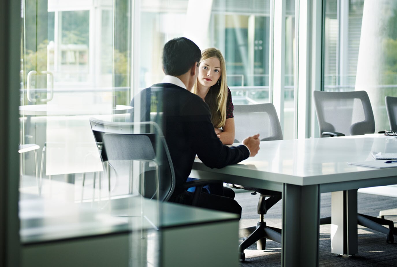 Two business people sitting at a table talk to each other.