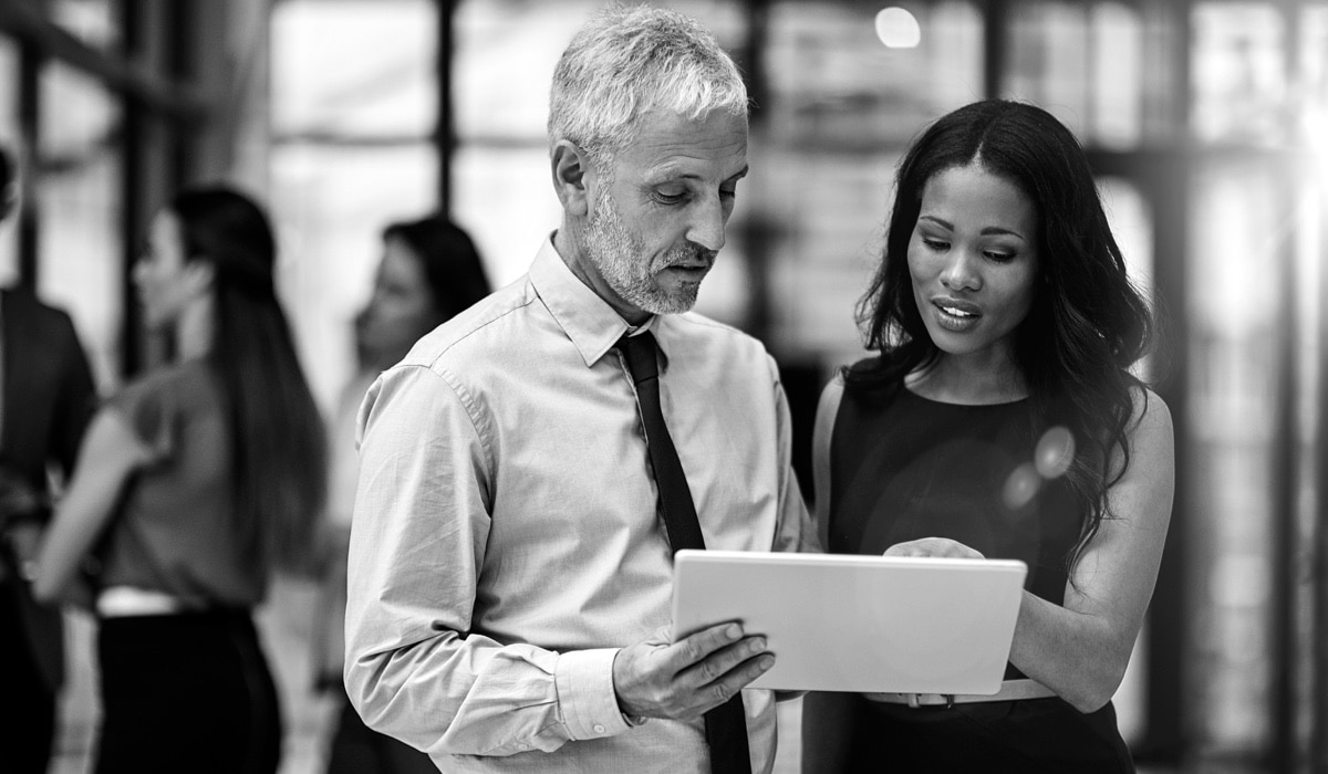 Two advisors stand in an office and review information on a tablet together.