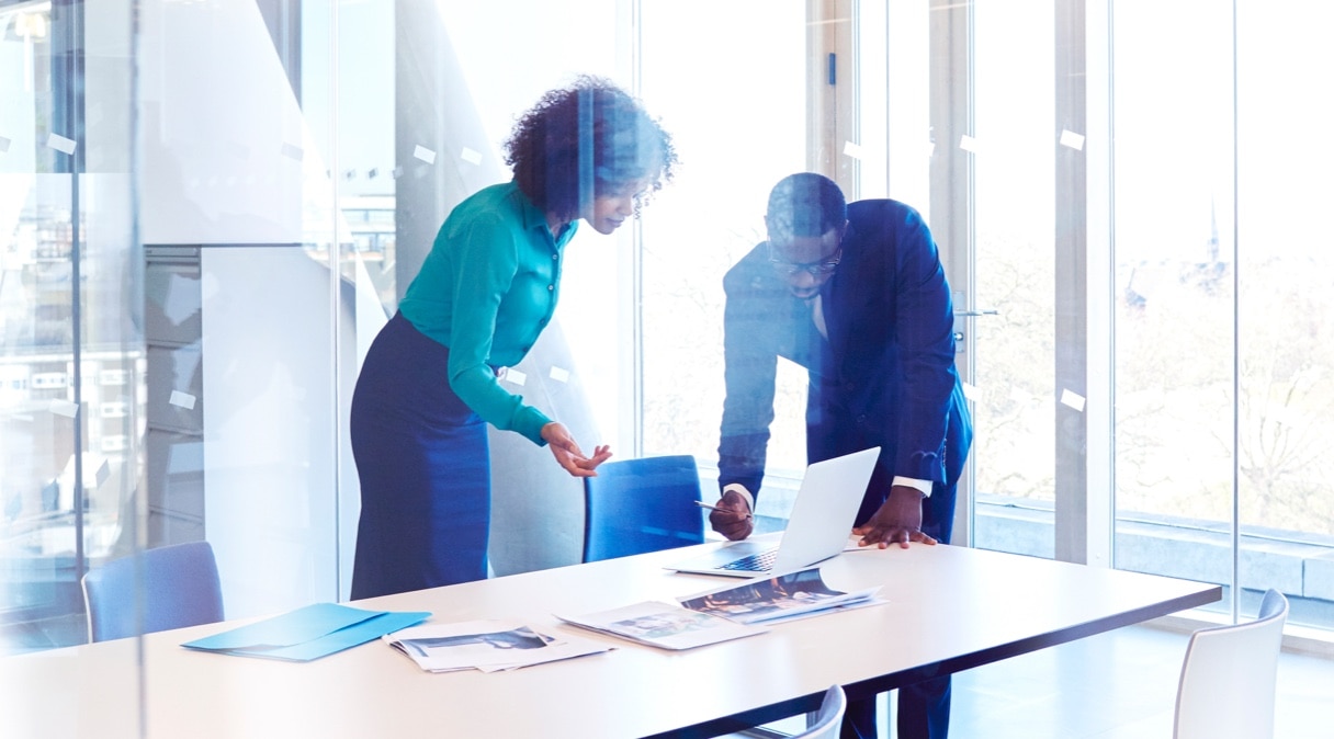 Two advisors stand over a table with a laptop and have a conversation.