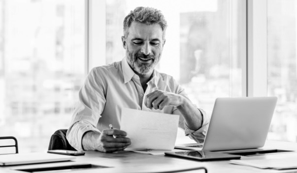A smiling businessperson looks at a paper while sitting at a desk with a computer.