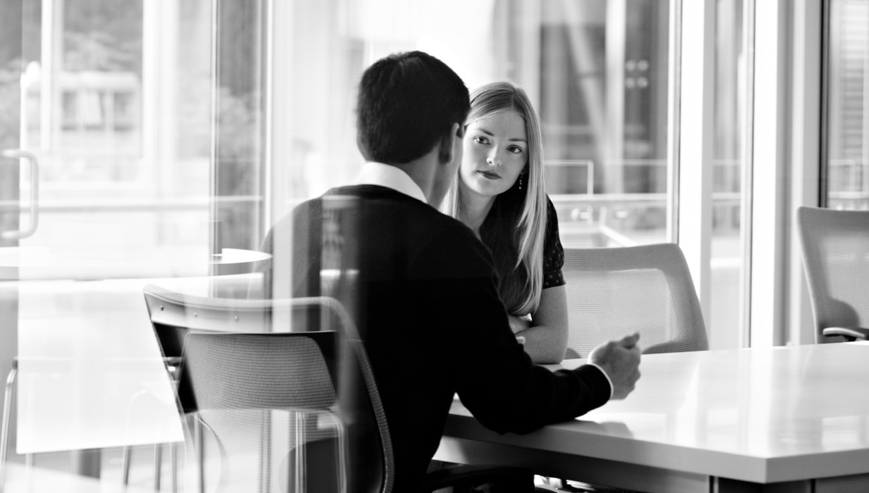 Two business people sitting at a table talk to each other.