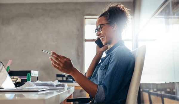 Woman sitting at desk on the phone and looking at paperwork with a pen in her hand.