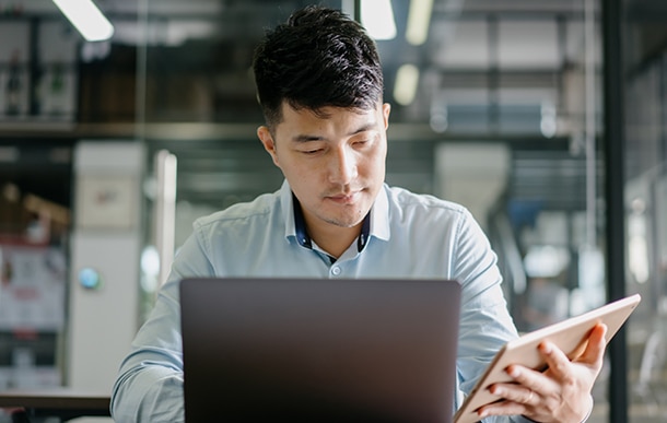 An advisor refers to his tablet while working on his laptop.